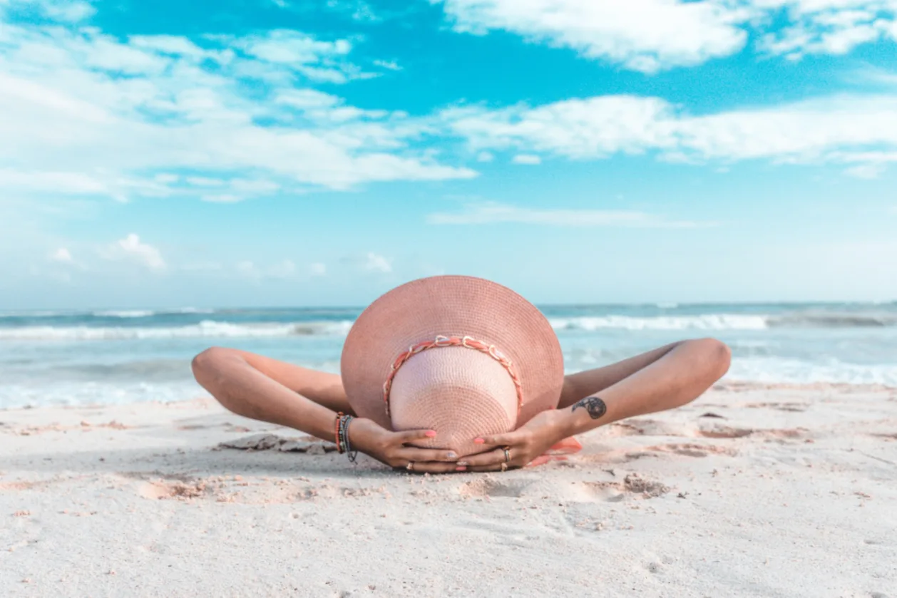 woman lounging on beach with straw sun hat